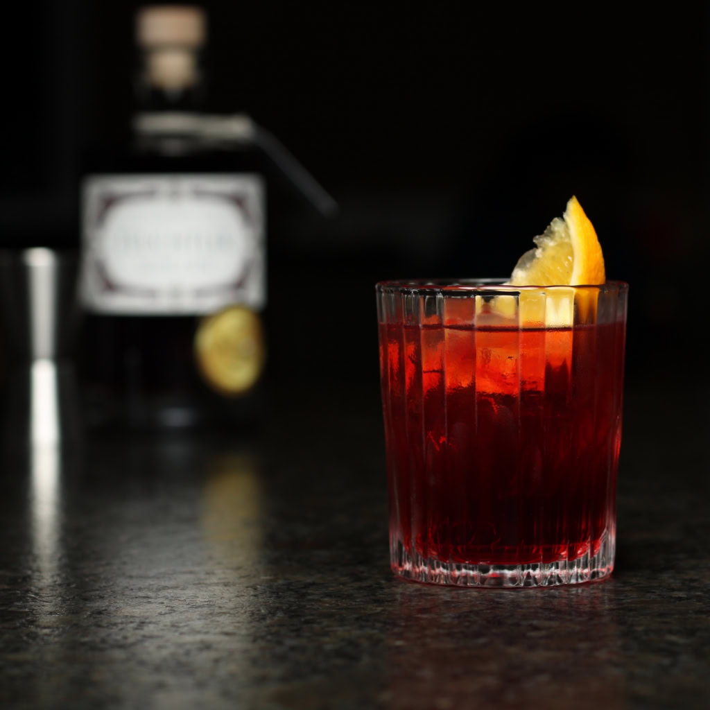 Sloe Negroni im geriffelten Glas mit Eiswürfeln, Orangenschnitz und leuchtend roter Farbe
