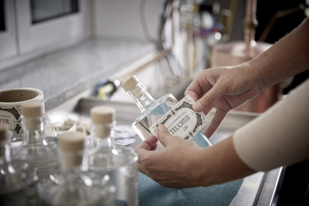 Hände bringen ein Teuchtler-Gin-Etikett auf einer Flasche an, weitere abgefüllte Flaschen stehen im Vordergrund.